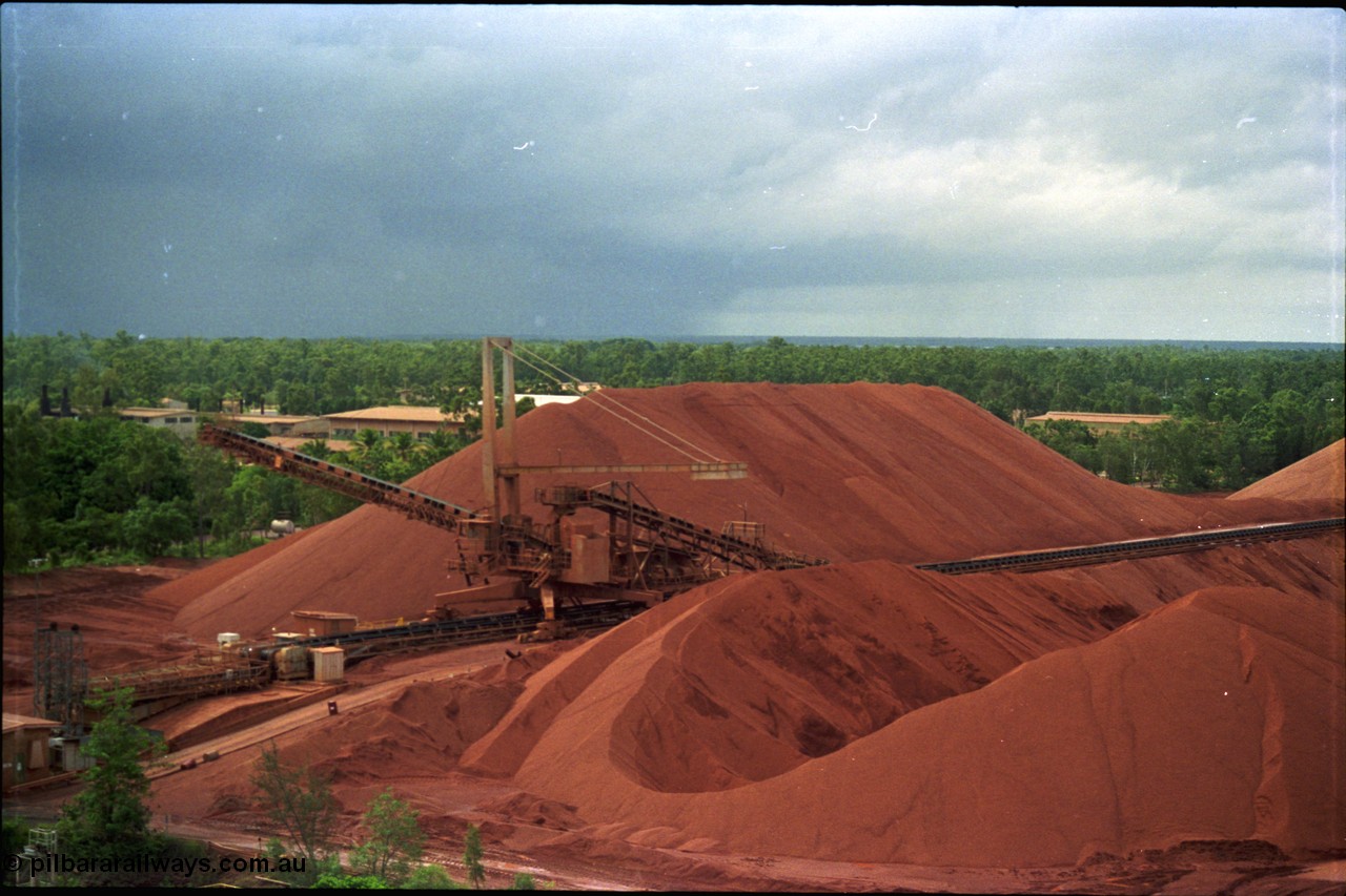 211-09
Weipa, Lorim Point stockpile area viewed from the wharf. A stacker is at the end of the yard belt with the reclaim tunnel for the wharf just visible at the bottom of frame.
