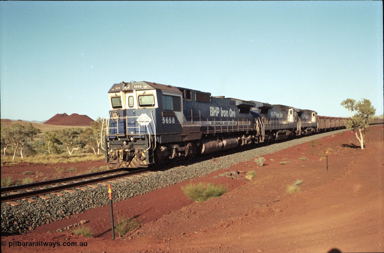 196-14
Yandi Two loaded car side of the loadout balloon loop, BHP Iron Ore CM40-8M or Dash 8 motive power in the form of 5658 'Kakogawa' serial 8412-03 / 94-149 rebuilt by Goninan as GE model CM40-8M from ALCo M636C number 5480 and two new Goninan built GE CM39-8 units 5630 'Zeus' serial 5831-09 / 88-079 and 5631 'Apollo' serial 5831-10 / 88-080 are the head end power with another two CM40-8M units mid-train. Train length is 240 waggons with a 120/120 split. Yandi Two ore stockpile and pedestal stacker boom tip visible in the background, the loadout operates via gravity and the train travels through a tunnel. May 1998.
Keywords: 5658;Goninan;GE;CM40-8M;8412-03/94-149;rebuild;AE-Goodwin;ALCo;M636C;5480;G6061-1;