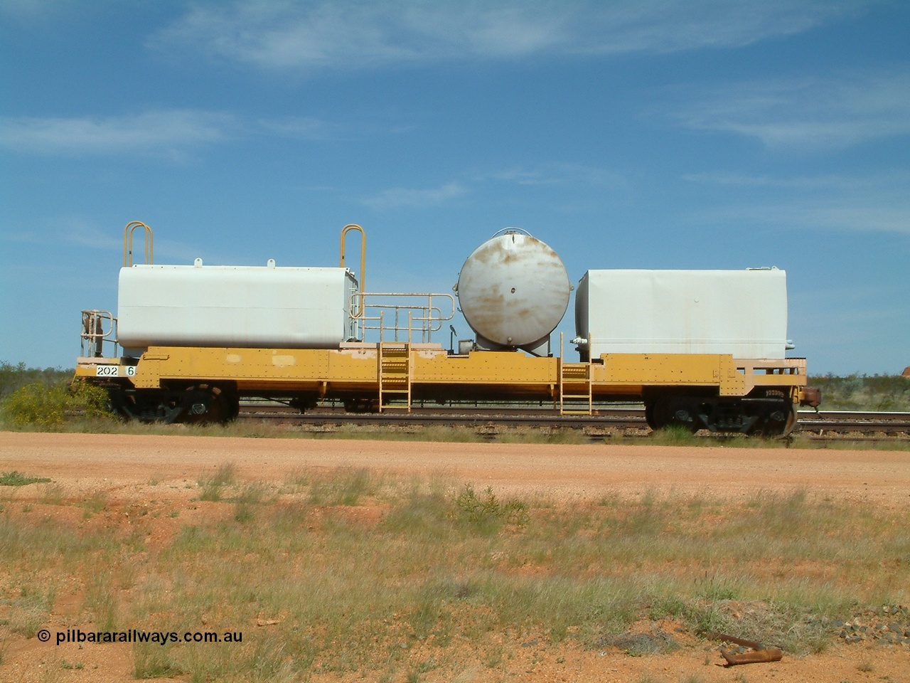 040419 102309
Abydos back track, riveted flat waggon 202 with three water tanks fitted, side view, shows access ladder profiles, originally part of the 'camp train', modified by Mt Newman Mining railway workshops.
Keywords: BHP-flat-waggon;