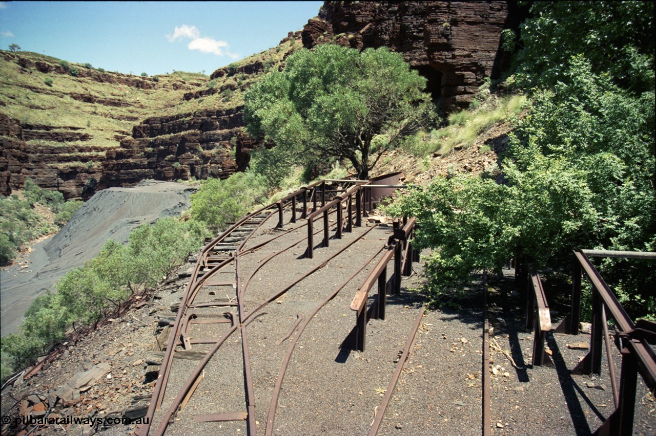 197-09
Wittenoom, Colonial Mine, asbestos mining remains, view looking south west of the open air locomotive storage roads with the battery off-take racks. The track used to continue around to the mine adits in the background.
