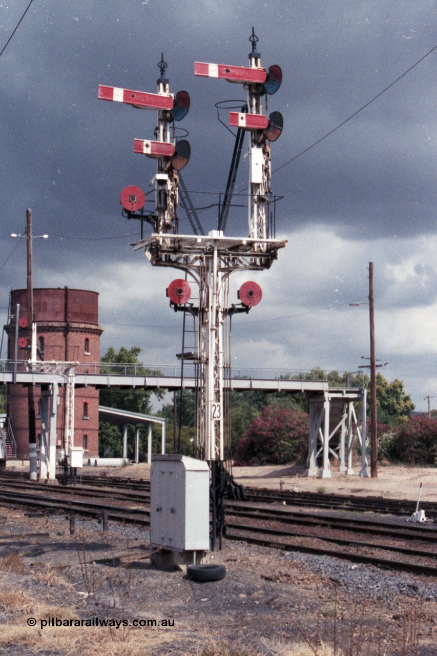 148-29
Wangaratta, Bracket Post 23, four arms and three Discs Up Signals, Top arm on Left-hand Doll Home Signal from Main Line to No.1 Road to Post 12. Bottom arm on Left-hand Doll Calling-on signal from Main Line to No. 1 Road towards Post 12. Disc on Left-hand Doll from Main Line to Siding 'A'. Top arm on Right-hand Doll Home Signal from Main Line to No. 2 Road to Post 14. Bottom arm on Right-hand Doll Calling-on Signal from Main Line to No.2 Road towards Post 14. Left-hand Disc on Post from Main Line to No. 2 Road towards Post 15. Right-hand Disc on Post from Main Line to No. 4 or 5 Roads towards Post 16. Footbridge, water tower and Disc Signal Post 21 in the background.
