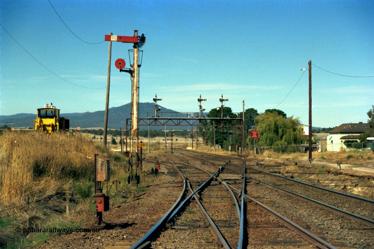 153-2-34
Ararat station yard overview looking towards Melbourne, tracks are from left, line to Maryborough, loco depot, main Western Line to Ballarat, line to Maroona, Semaphore signal and disc post 7, telephone cabinet and point indicators, signal gantry has post 4, 5 and 6, double disc post in background is post 3 from loco depot, point rodding can be seen at right crossing drain, ballast regulator at left.
