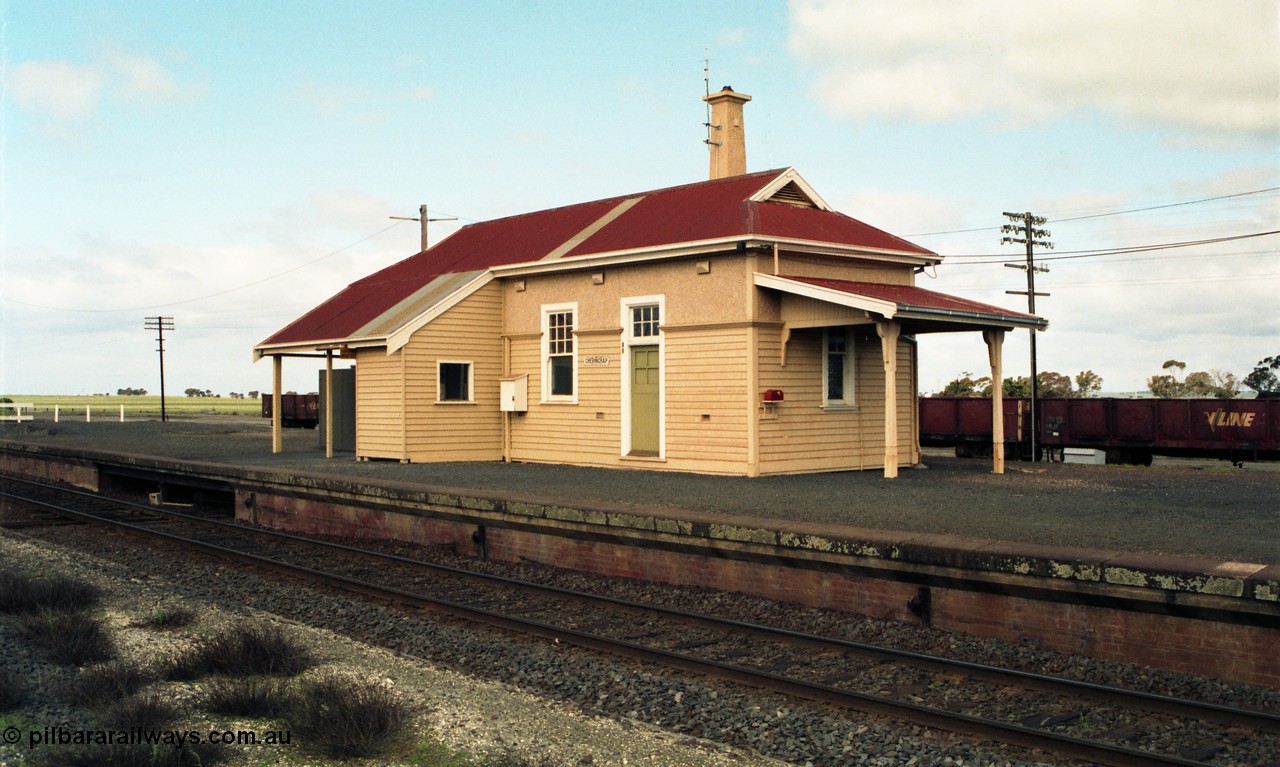 154-00
Gheringhap station building overview, platform and coping, taken from site of former No.2 platform, staff exchange box visible, gypsum waggons in yard behind station building.
