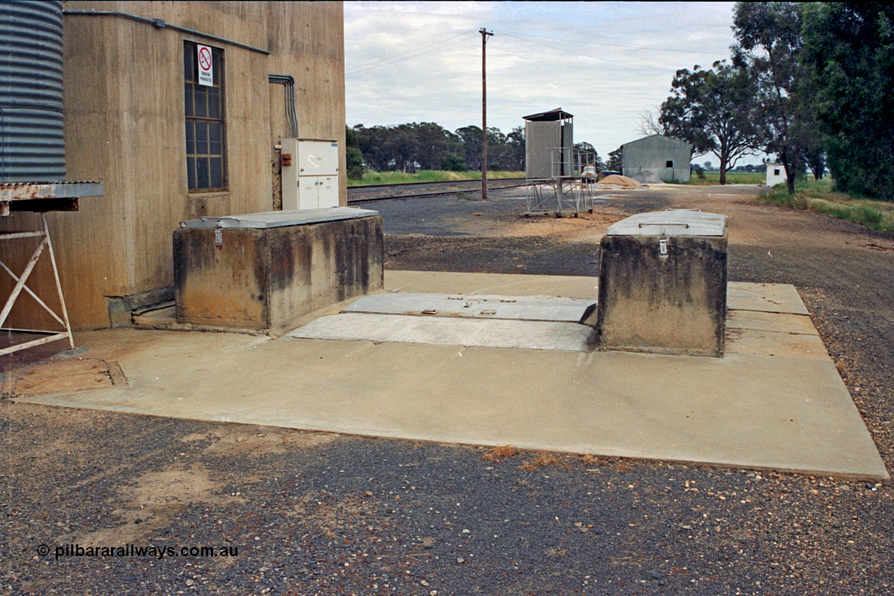 175-23
Pine Lodge, view of road receival point, or truck unloading dump point for a Williamstown style silo complex, GEB sampling gantry, with super phosphate shed in the background, road vehicle weighbridge visible on the right.
