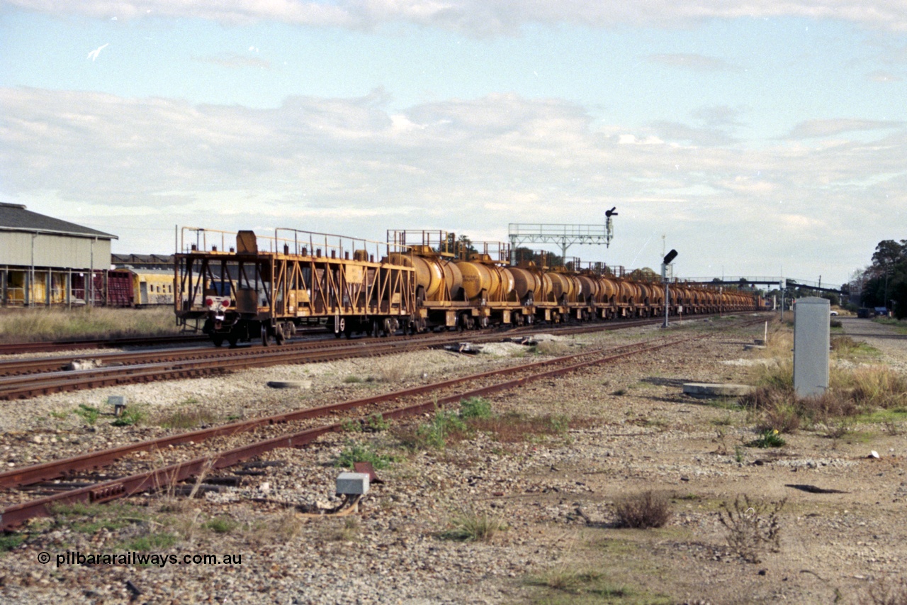 186-03
Midland, trailing view of the standard gauge up Kalgoorlie acid train 428, showing the 28 CSA type tanks on WQH type bogie flat waggons with an WMX type bogie car carrying waggon as the rear barrier waggon, Midland Workshops behind train.
Keywords: WQH-type;CSA-type;WMX-type;