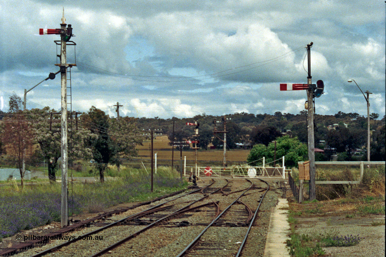 192-36
Cootamundra West, NSW, looking east in the up direction along the Main Line from the platform with the Loop Line on the left and across the partially removed scissors crossover and the non-interlocked crossing gates for Yass Road. The lower quadrant semaphore signal on the left is operated by lever 42 while the right one is operated by lever 40. The facing signal right at the road crossing is controlled by Cootamundra North Signal Box, the down facing signals are from levers 6 Goulburn to Main Line and 14 Goulburn to Loop Line.

