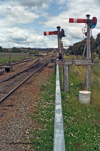 192-28
Cootamundra West, NSW, view looking east in the up direction of the reduced height mechanical lower quadrant semaphore signals due to the airport beside the line, the left doll is operated by lever 43 and is for the Temora to Loop Line while the right is lever 47 and for the Temora to Main Line or South Fork. Frame B is visible on the left and the clearance bar on the main can be seen. The concrete footing is for a future electric light signal installation.
