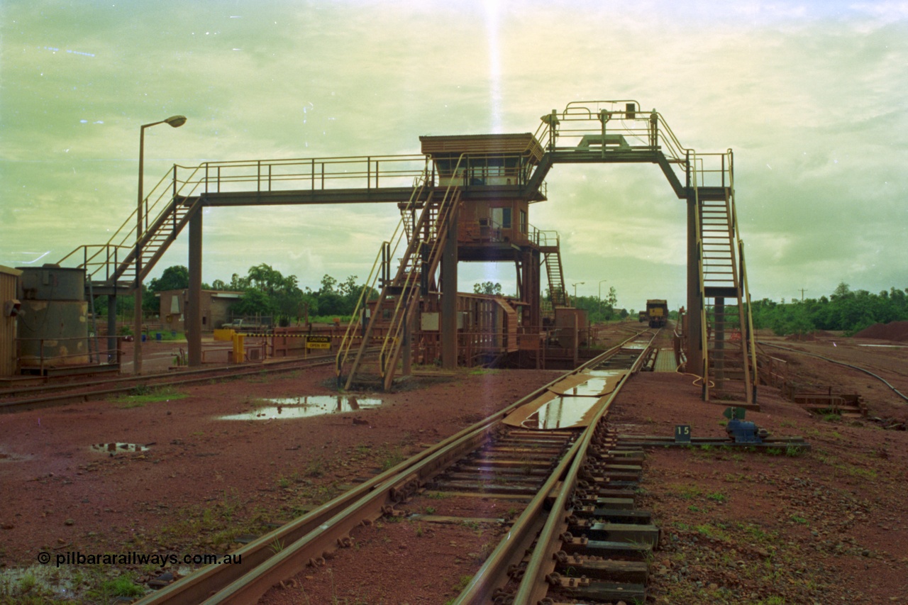 210-04
Weipa, Lorim Point, Comalco rail dump station, view looking towards the workshops, shows inspection walkway and opening for unloading hopper, control cabin, the waggons are discharged on the left track behind the OPEN PIT sign.

