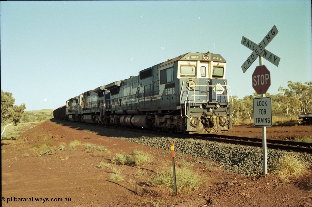 196-03
Yandi Two loaded car side of the loadout balloon loop, BHP Iron Ore CM40-8M or Dash 8 motive power in the form of 5658 'Kakogawa' serial 8412-03 / 94-149 rebuilt by Goninan as GE model CM40-8M from ALCo M636C unit 5480 and two new Goninan built GE CM39-8 units 5630 'Zeus' serial 5831-09 / 88-079 and 5631 'Apollo' serial 5831-10 / 88-080 are the head end power with another two CM40-8M units mid-train. Train length is 240 waggons with a 120/120 split. Yandi Two ore stockpile and pedestal stacker boom tip visible in the background, the loadout operates via gravity and the train travels through a tunnel. May 1998.
Keywords: 5658;Goninan;GE;CM40-8M;8412-03/94-149;rebuild;AE-Goodwin;ALCo;M636C;5480;G6061-1;
