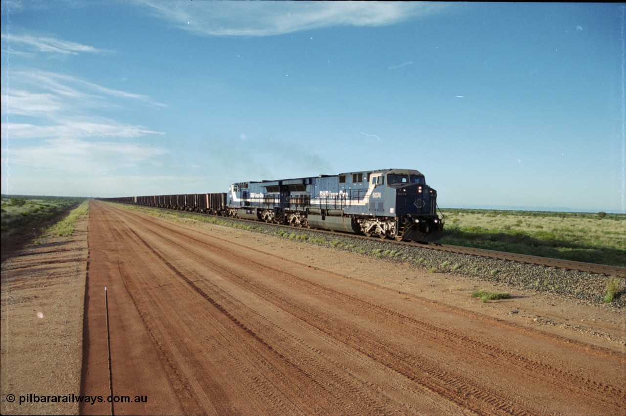 225-19
At the 24.1 km grade crossing on the BHP Newman line, the afternoon departure for Yandi mine heads south behind the standard double General Electric AC6000 units with GE Erie built 6074 serial 51066 leading sister unit 6075 with another AC6000 unit mid-train. This was before the units were named. [url=https://goo.gl/maps/qGkyfiuy6212]GeoData[/url].
Keywords: 6074;GE;AC6000;51066;