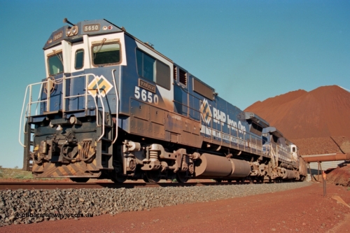 229-23
Yandi Two loadout, looking at the exit portal of the tunnel as Goninan rebuild CM40-8M GE unit 5650 'Yawata' serial 8412-07 / 93-141 drags a loading train through at 1.2 km/h, the massive pile of ore is gravity fed into the waggons via two sets of hydraulic chutes, the original pedestal radial stacker is visible above the ore along with the extraction fan. [url=https://goo.gl/maps/jmtnauf76Zq]GeoData[/url].
Keywords: 5650;Goninan;GE;CM40-8M;8412-07/93-141;rebuild;AE-Goodwin;ALCo;M636C;5481;G6061-2;