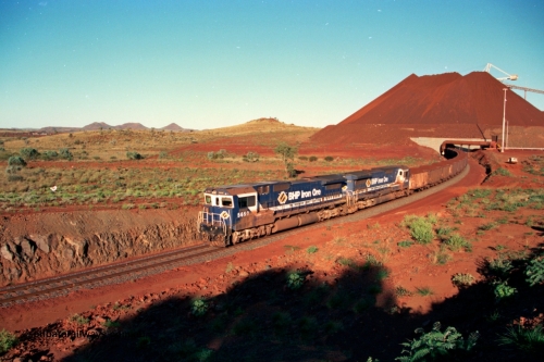 229-30
Yandi Two loadout exit side, as Goninan rebuild CM40-8M GE unit 5650 'Yawata' serial 8412-07 / 93-141 and sister unit drag a loading train at 1.2 km/h, the massive pile of ore is gravity fed into the waggons via two sets of hydraulic chutes, the original pedestal radial stacker is visible above the ore along with the extraction fan, on the left the mid-train remotes can just be made out. [url=https://goo.gl/maps/KQ3dQNrTwd42]GeoData[/url].
Keywords: 5650;Goninan;GE;CM40-8M;8412-07/93-141;rebuild;AE-Goodwin;ALCo;M636C;5481;G6061-2;
