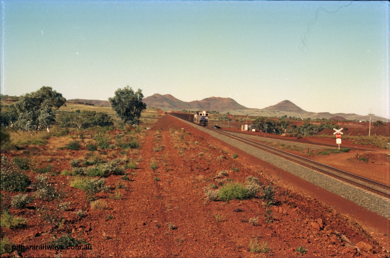 230-04
Yandi Two switch looking east with the Three Sisters forming the background. Empty BHP train heading for the balloon loop for loading, grade crossing is the YT 311.5 km. Geodata [url=https://goo.gl/maps/DcycDGojcBt] -22.713725, 119.055762 [/url].
