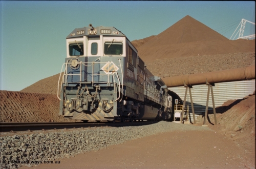 230-17
Yandi Two load-out tunnel exit side portal, Goninan rebuild GE CM40-8M model 5654 'Kashima' serial 8412-11/93-145 leads a loading train 1.2 km/h. The ore stockpile and pedestal stacker are visible. The livery is the marigold version of the BHP Australia logo. Geodata [url=https://goo.gl/maps/h68ia1caJvL2] -22.718338, 119.039909 [/url].
Keywords: 5654;Goninan;GE;CM40-8M;8412-11/93-145;rebuild;Comeng-NSW;ALCo;M636C;5493;C6084-9;