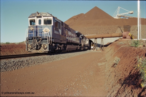 230-19
Yandi Two load-out tunnel exit side portal, Goninan rebuild GE CM40-8M model 5654 'Kashima' serial 8412-11/93-145 leads a loading train 1.2 km/h. The ore stockpile and pedestal stacker are visible. The pipe and fan are for the dust extraction system. The livery is the marigold version of the BHP Australia logo. Geodata [url=https://goo.gl/maps/h68ia1caJvL2] -22.718338, 119.039909 [/url].
Keywords: 5654;Goninan;GE;CM40-8M;8412-11/93-145;rebuild;Comeng-NSW;ALCo;M636C;5493;C6084-9;