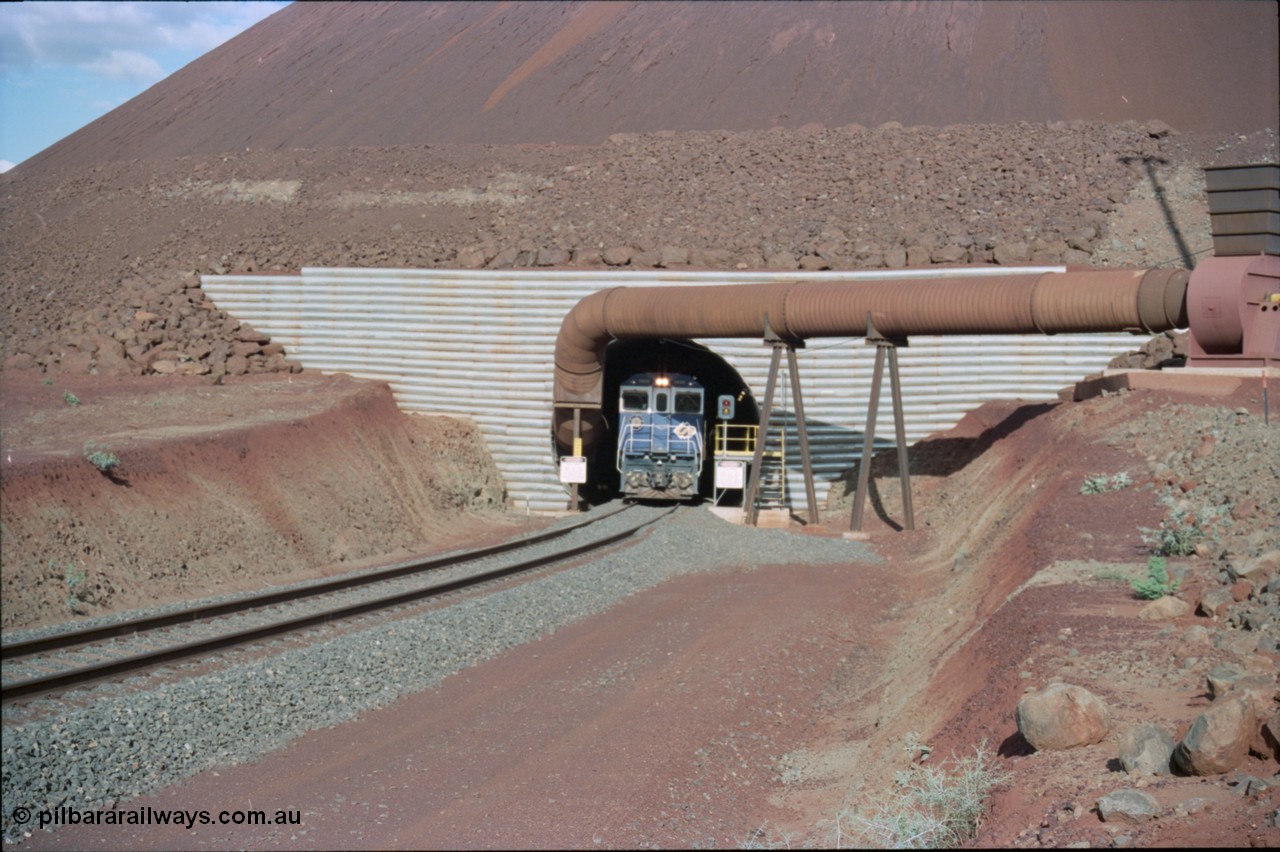 233-07
Yandi Two exit portal or loaded car side of load-out tunnel, the Yandi Two load-out has two load-out stations or vaults to allow to different products to be loaded. Only one vault is used at a time. A loading train lead by BHP Iron Ore's Goninan rebuild CM40-8M GE unit 5650 'Yawata' serial 8412-07 / 93-141 as it drags the train through at 1.2 km/h. [url=https://goo.gl/maps/RgJfYGtPXb52]GeoData[/url].
