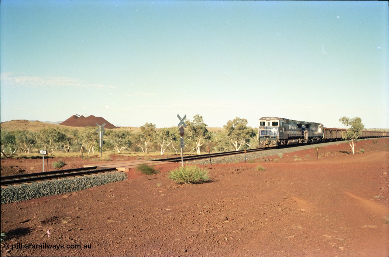 234-32
Yandi Two, BHP Iron Ore Goninan rebuild CM40-8M GE unit 5658 'Kakogawa' serial 8412-03 / 94-149 on the front of a 240 waggon loaded train, this configuration was trialled for a time with two Dash 8 locos, 120 waggons, Dash 8, 120 waggons and Dash 8. View looking across the YT315.8 km grade crossing and 5658 back to the ore stockpile at the loadout. Circa 1998.
Keywords: 5658;Goninan;GE;CM40-8M;8412-03/94-149;rebuild;AE-Goodwin;ALCo;M636C;5480;G6061-1;