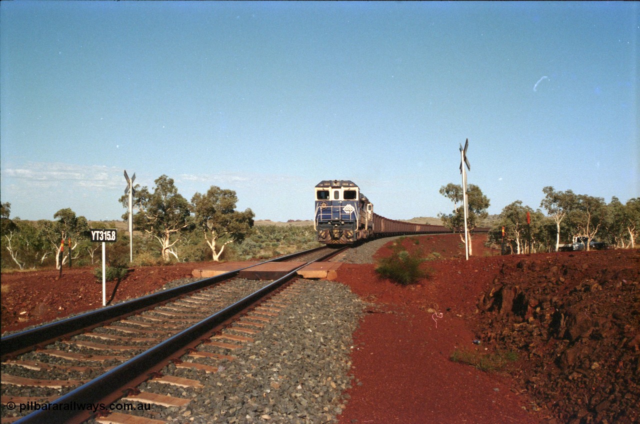 234-33
Yandi Two, BHP Iron Ore Goninan rebuild CM40-8M GE unit 5658 'Kakogawa' serial 8412-03 / 94-149 on the front of a 240 waggon loaded train, this configuration was trialled for a time with two Dash 8 locos, 120 waggons, Dash 8, 120 waggons and Dash 8. View looking across the YT315.8 km grade crossing and 5658 back to the ore stockpile at the loadout. Circa 1998.
Keywords: 5658;Goninan;GE;CM40-8M;8412-03/94-149;rebuild;AE-Goodwin;ALCo;M636C;5480;G6061-1;