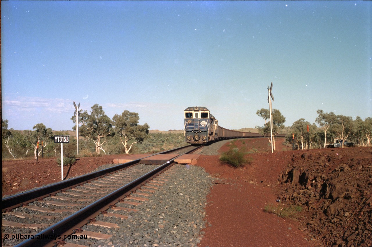 234-34
Yandi Two, BHP Iron Ore Goninan rebuild CM40-8M GE unit 5658 'Kakogawa' serial 8412-03 / 94-149 on the front of a 240 waggon loaded train, this configuration was trialled for a time with two Dash 8 locos, 120 waggons, Dash 8, 120 waggons and Dash 8. View looking across the YT315.8 km grade crossing and 5658 back to the ore stockpile at the loadout. Circa 1998.
Keywords: 5658;Goninan;GE;CM40-8M;8412-03/94-149;rebuild;AE-Goodwin;ALCo;M636C;5480;G6061-1;
