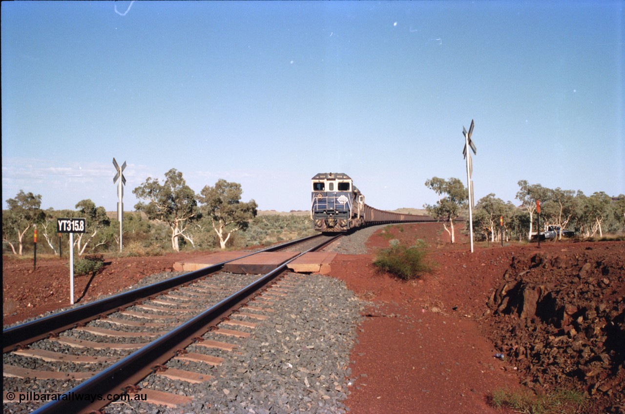 234-37
Yandi Two, BHP Iron Ore Goninan rebuild CM40-8M GE unit 5658 'Kakogawa' serial 8412-03 / 94-149 on the front of a 240 waggon loaded train, this configuration was trialled for a time with two Dash 8 locos, 120 waggons, Dash 8, 120 waggons and Dash 8. View looking across the YT315.8 km grade crossing and 5658 back to the ore stockpile at the loadout. Circa 1998.
Keywords: 5658;Goninan;GE;CM40-8M;8412-03/94-149;rebuild;AE-Goodwin;ALCo;M636C;5480;G6061-1;
