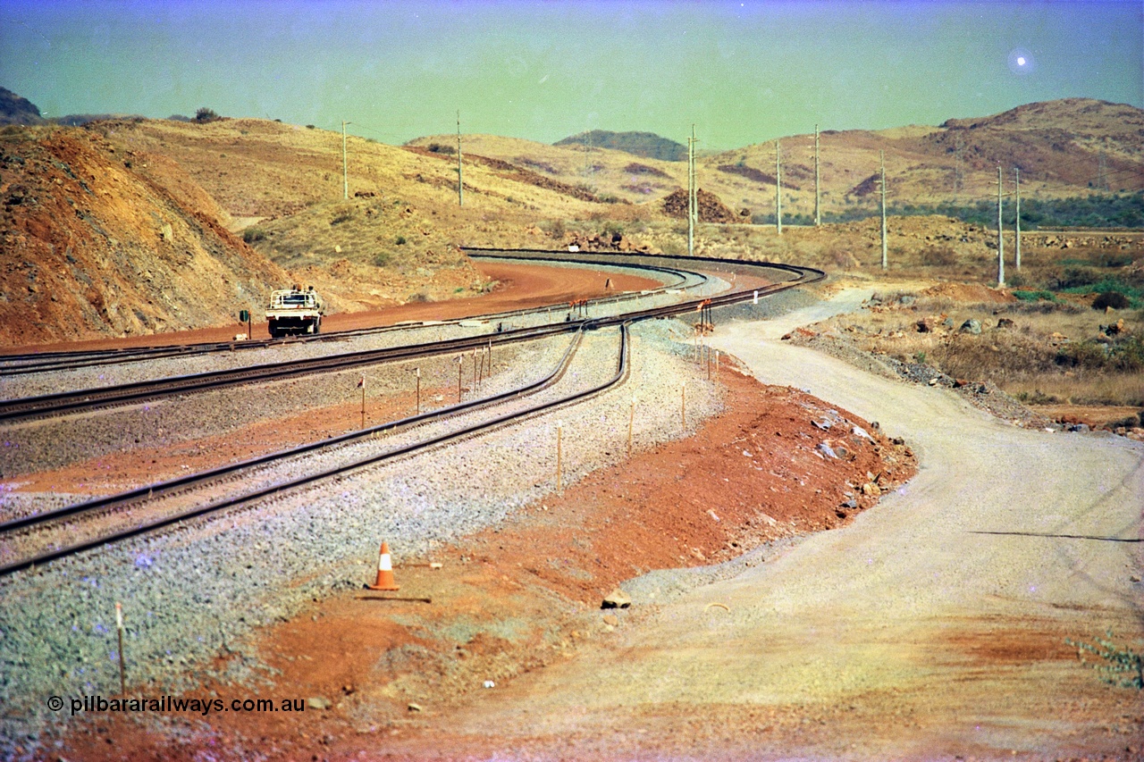 246-03
Cape Lambert, yard view of the then new extension to the south for the West Angelas mine was coming on stream, the just visible siding (rejoining) on the far left will become a compressor waggon holding road, the 6 km and Boat Beach Rd grade crossing are around the corner to the left. Closest to the camera is the extended No. 1 Road which becomes the Empty Car Line from car dumper one for the Deepdale traffic. Next is the original line or Mainline and the third line across is the Loaded Car Line for the West Angelas traffic to the new car dumper 2. 22nd May 2002.
