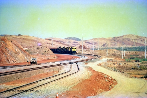 246-07
Cape Lambert, yard view of the then new extension to the south for the West Angelas mine was coming on stream as a Robe River loaded Deepdale train arrives on the main behind the standard quad Dash 8 power with 202 waggons, the just visible siding (rejoining) on the far left will become a compressor waggon holding road, the 6 km and Boat Beach Rd grade crossing are around the corner to the left. Closest to the camera is the extended No. 1 Road which becomes the Empty Car Line from car dumper one for the Deepdale traffic. Next is the original line or Mainline and the third line across is the Loaded Car Line for the West Angelas traffic to the new car dumper 2. 22nd May 2002.
