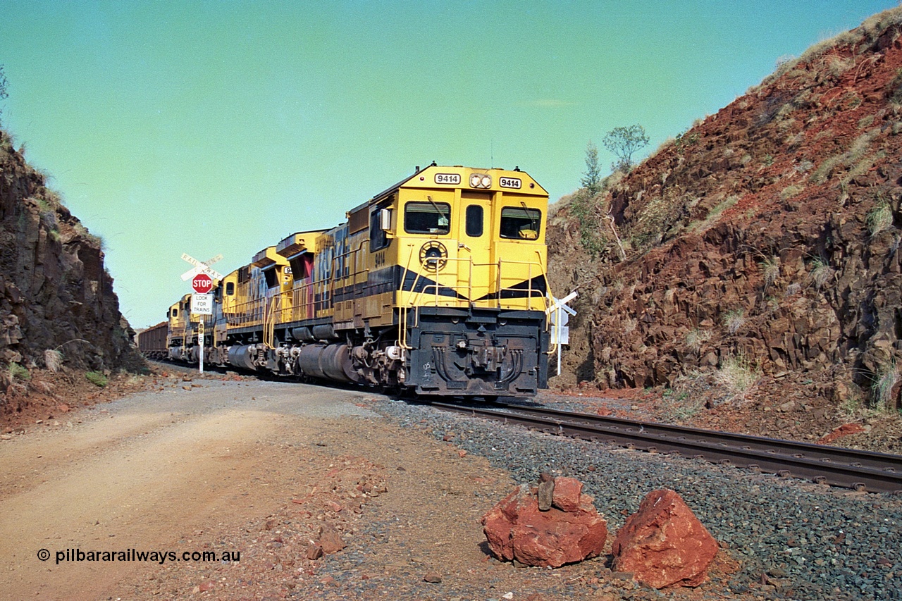 256-33
At the 89.6 km grade crossing the loaded train behind the quad CM40-8M working of 9414, 9420, 9410 and 9425 rolls across the crossing and heads down the 1.26 percent grade. 9414 was built by AE Goodwin NSW as an ALCo M636 model in December 1971 with serial number G-6060-5 and part of the original order for five units. Locomotive was delivered to Robe River in January 1972 with Bechtel Pacific road umber 262.005 for construction use and was renumbered 1714 when that was completed. 9414 was rebuilt by Goninan WA in November 1991 to become an CM40-8M model with serial number 8206-11 / 91-124. May 2002.
Keywords: 9414;Goninan;GE;CM40-8M;8206-11/91-124;rebuild;AE-Goodwin;ALCo;M636;G6060-5;