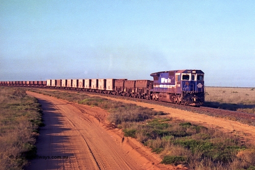 257-25
Goldsworthy Junction, an empty train runs between the junction and the Broome Rd crossing behind the standard single locomotive 5646 'White Springs', a Goninan 1992 built GE CM40-8 model with serial number 5244-11 / 92-135. The four styles of waggon in use are visible, behind the loco are three Golynx waggons, then a number of Gunderson USA builds, the ribbed type is a Portec USA built and then following are the Tomlinson WA and Scotts of Ipswich built 70 ton waggons. Late 2001.
Keywords: 5646;Goninan;GE;CM40-8;8244-11/92-135;