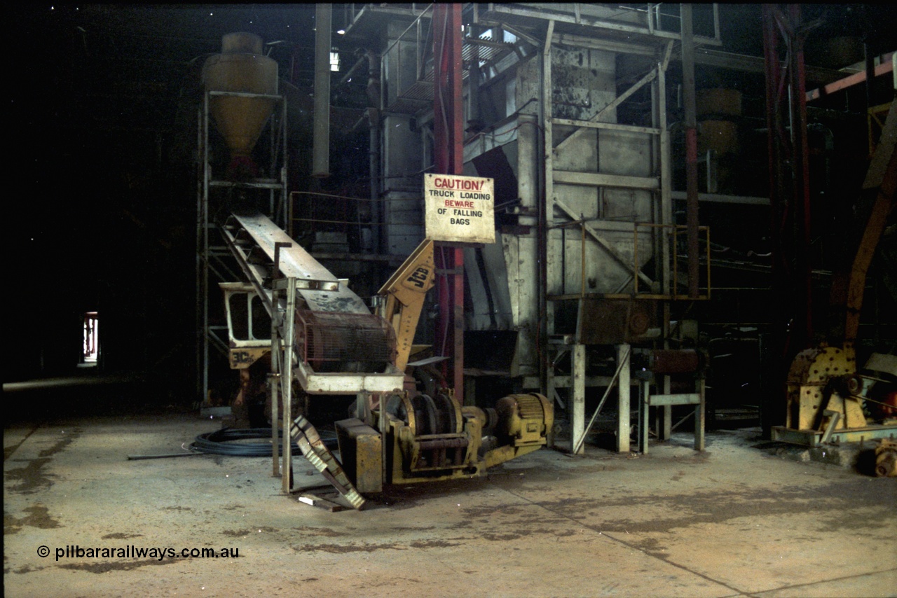 195-24
Wittenoom Gorge, Australian Blue Asbestos or ABA Colonial Mill, view inside part of the bagging plant within the mill, near the truck loading area, JCB backhoe can be seen behind conveyor.
