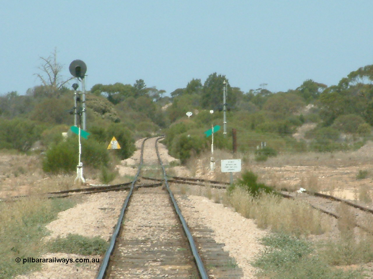 030405 140102
Kyancutta, yard view looking south along the narrow gauge mainline with the siding point levers and indicators with the Eyre Highway grade crossing and one of only three electrically lit signals on the Eyre Peninsula Division. The cast iron 'Yard Limit' sign can be made out in the distance, 5th April 2003.
