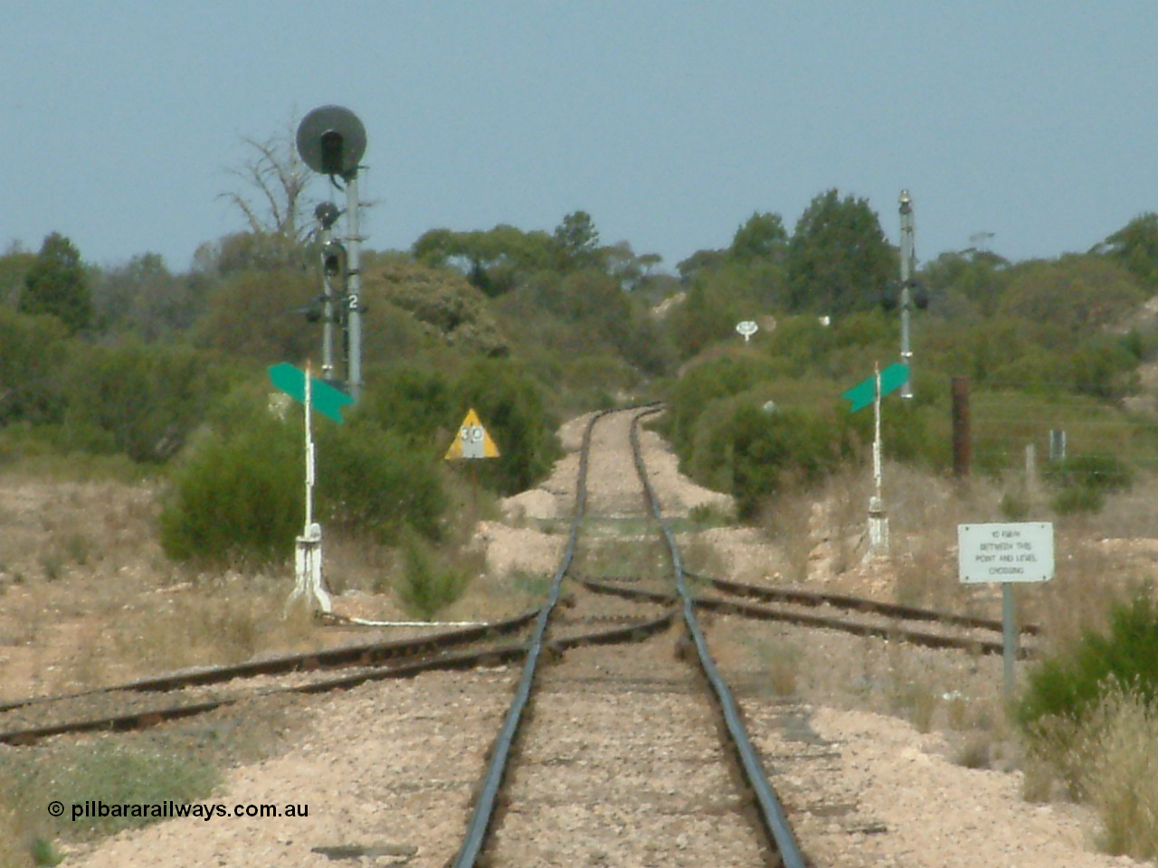 030405 140546
Kyancutta, yard view looking south along the narrow gauge mainline with the siding point levers and indicators with the Eyre Highway grade crossing and one of only two electrically lit signals on the Eyre Peninsula Division. The cast iron 'Yard Limit' sign can be made out in the distance, 5th April 2003.
