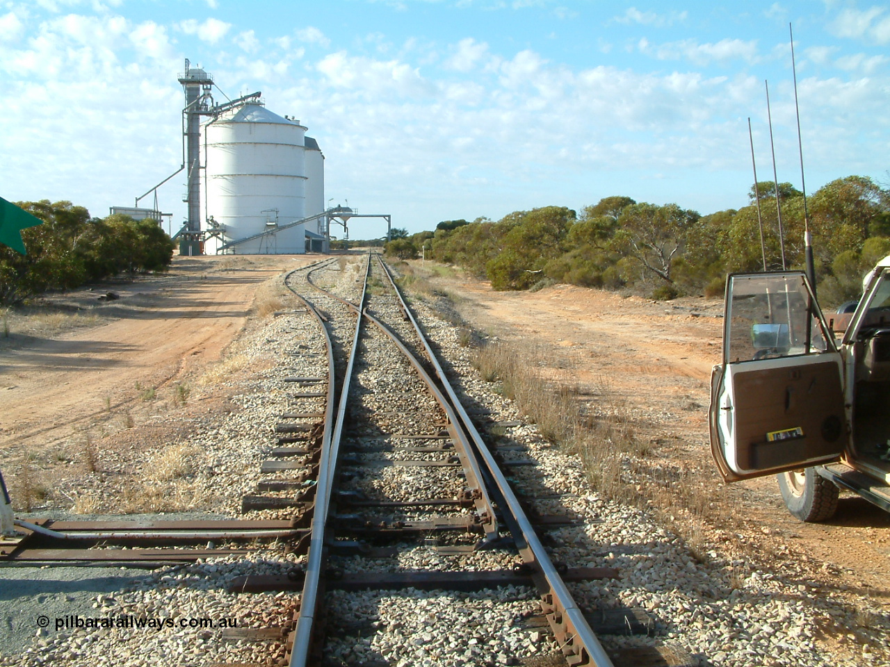 030406 082324
Murdinga, yard overview looking south down the mainline from the north end, with grain siding and silo complex with outflow spout on gantry over both tracks. 6th April 2003.
