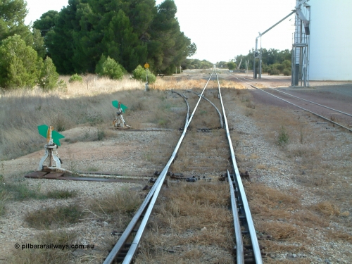 030406 092313
Yeelanna, station yard view looking north down the mainline from the south end of the station siding, points, leaver and indicator for the Kapinnie and former Mount Hope line at the bottom of frame, then the south end points, lever and indicator for the station siding, and then the high yellow disk for the southern leg of the triangle can be seen. With silo outflow spouts on the right. 6th April 2003.
