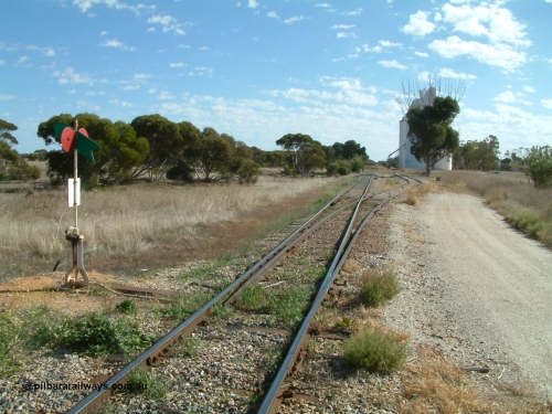 030406 093000
Yeelanna, station located at the 81.7 km, original terminus of line in April 1909, then junction for line to Mount Hope in October 1914. Station yard overview from the south end looking north, points, lever and indicator for the grain siding with concrete silo complexes in the background. The branch line to Kapinnie and former Mount Hope is just visible through the trees on the raised embankment. 6th April 2003.

