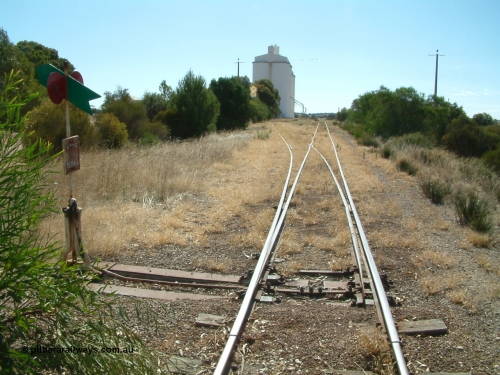 030406 142638
Kapinnie, station located at the 105 km, this is the second location and in use from 1954. Station yard overview looking west with point lever and indicator and concrete silo complexes and outflow spouts. April 6, 2003.
