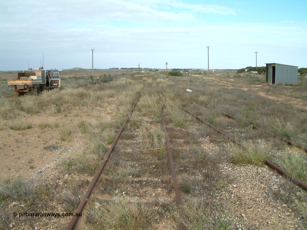 030414 154350
Penong, 505.6 km looking east with the goods loop coming in on the right to join the mainline. The car is on the grain loop. Station shelter on the right is where the original barracks were located.
