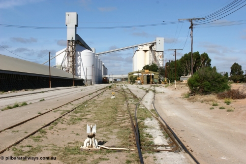 060113 2459
Thevenard, yard view looking west from No. 13 points at the front of the maintenance 'yard' with the disused grain bunker and 6DD3 running along beside the silos as it unloads at GRA, further silos form the background with the maintenance centre with stand-by loco 871 on hand and a couple of ENH hopper waggons. 13th January 2006.
