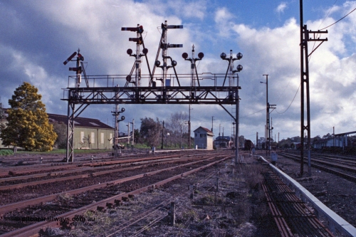 103-23
Benalla station yard overview, signal gantry still complete and intact, semaphore signal post 28 pulled off for up Albury pass, looking south, before rationalisation, workshops at left, Benalla B signal box, point rodding and signal wires, Freightgate canopy at right.

