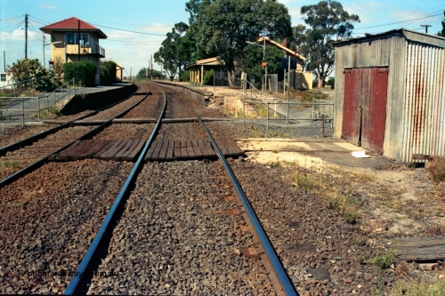 105-14
Wallan station overview, looking south from down line, elevated signal box and up platform on the left, gangers trolley shed, crib crossing and station building.
