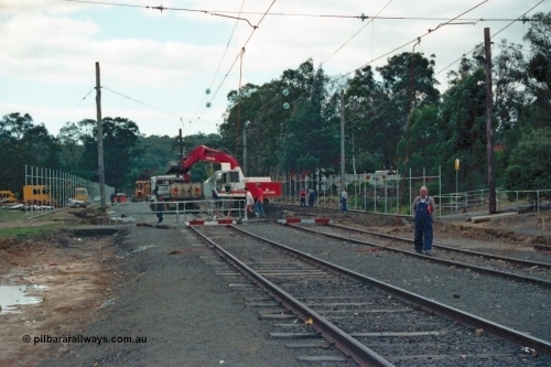 115-05
Hurstbridge, looking north from existing stabling tracks with overhead traction wire grounded, timber traction poles, looking through crib crossing, points on right have been removed, even though Hurstbridge is a terminus a flagman is still present to protect the gang.
