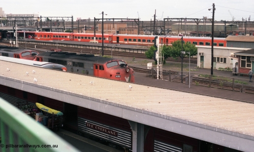 116-08
Spencer Street Station, view looking west from flyover, V/Line broad gauge A class light engines A 81 and A 62 run towards platform No.3, 'The Overland' Motorail waggons on platform No.2, DERMs 55 RM and 54 RM at left, West Tower in the middle background, Spencer Street No.1 Signal Box at right with broad gauge passenger stabling and maintenance sidings behind it, track work, points, searchlight signals and gantries and shunting signals.
