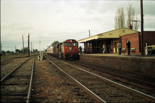117-11
Springhurst, V/Line N class N 466 'City of Warrnambool' Clyde Engineering EMD model JT22HC-2 serial 86-1195 arrives with an N set and D van on an up Albury passenger train as the driver and signaller exchanges electric staffs, yard overview, station building and platform.
Keywords: N-class;N466;Clyde-Engineering-Somerton-Victoria;EMD;JT22HC-2;86-1195;