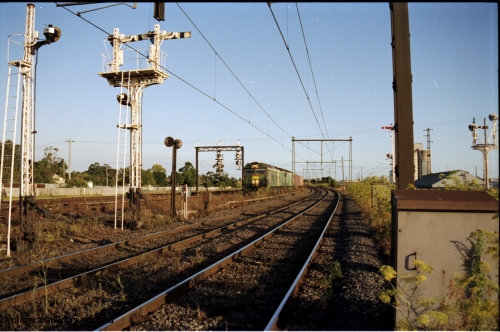 124-15
Sunshine looking from the passenger lines across to the Independent Through Goods lines, signal post 71 at camera, disc and semaphore signal posts 31 and 31B for control of the Independent Trough Goods lines, down Adelaide broad gauge goods train waiting to cross over the passenger lines, BL classes BL 30 Clyde Engineering EMD model JT26C-2SS serial 83-1014 and BL 35 Clyde Engineering EMD model JT26C-2SS serial 83-1019 in AN livery, standard gauge Sunshine Loop to the left of train, Newport Loop Line and GEB sidings at far right
