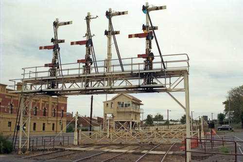 128-04
Ballarat station, view of elevated Ballarat B or Lydiard Street Signal Box, interlocked gates and semaphore signal gantry with semaphore signal Posts 26 and 27 Up signals removed, Post 28 facing away and Post 29, looking west across crib pedestrian crossing, Provincial Hotel on the left.
