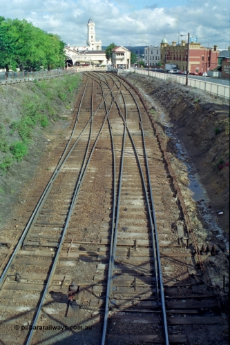 139-16
Ballarat station junction, track view of the junction at Ballarat B signal box or Lydiard Street box, looking east from the Armstrong Street bridge, double track to triple track which used to then become four tracks on the other side of the gates before No. 2 Road was removed. The shadow of Disc Post 33 can be seen along with the interlocking of the points with the signal pulleys.
