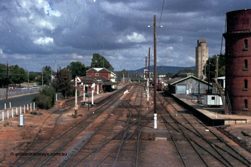 143-01
Wangaratta station yard overview looking south from footbridge, the broad gauge down Wahgunyah Special mixed train 'Stringybark Express' arrives and the signal man swaps electric staffs with the crew, the 18th century infrastructure clearly on display here, semaphore signal Post 20 is pulled off for departure, station building and platform, elevated signal box, signal posts and interlocking, goods shed and water tower.
