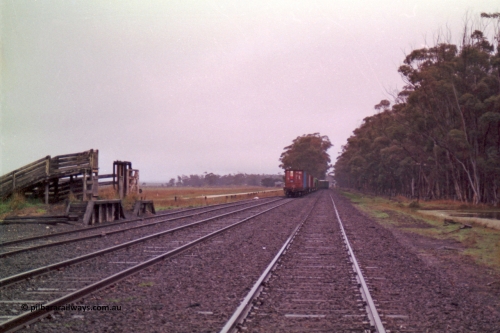 150-18
Lismore, station yard and stock loading race, sheep race closest to camera with cattle race behind, looking towards Maroona from No. 1 road, V/Line broad gauge Adelaide bound goods train 9169 exiting No. 2 and re-joining the mainline through the trailable points.
