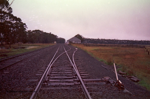 150-20
Lismore station yard overview from Maroona end of goods loop looking east, station building at left on No. 1 road, taken from goods loop points on No.2 road, point lever, stock yards and races with grain bunker behind.
