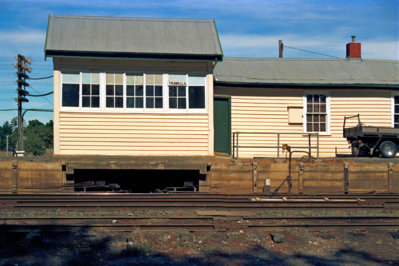 153-2-20
Trawalla signal box and automatic electric staff exchange apparatus setup with staff for an up train, point rodding and signal wires leaving the platform, levers visible in windows.
