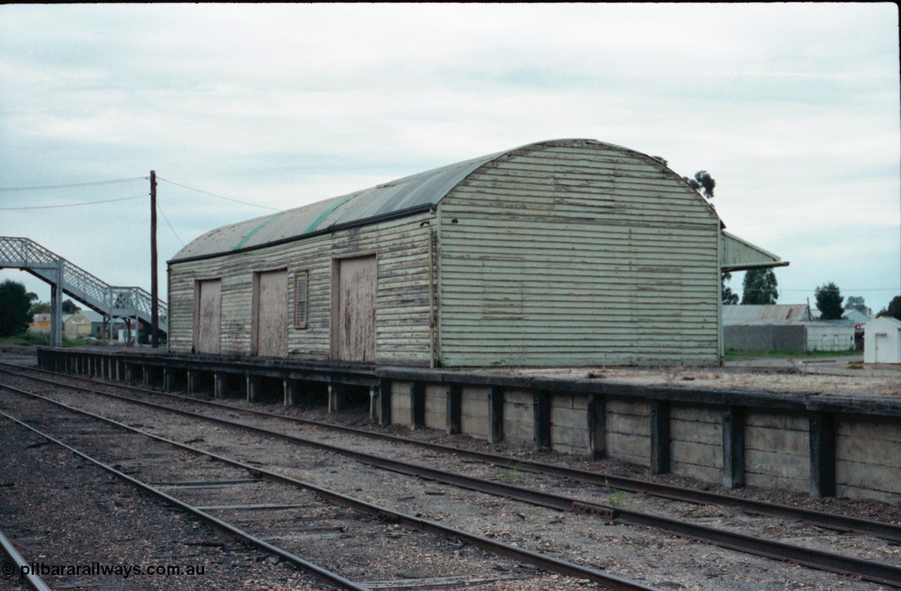 161-04
Numurkah, yard view of goods shed with curved roof and goods loading platform, steel lattice footbridge at end of platform, white build at far right is the road vehicle weighbridge scale room.
